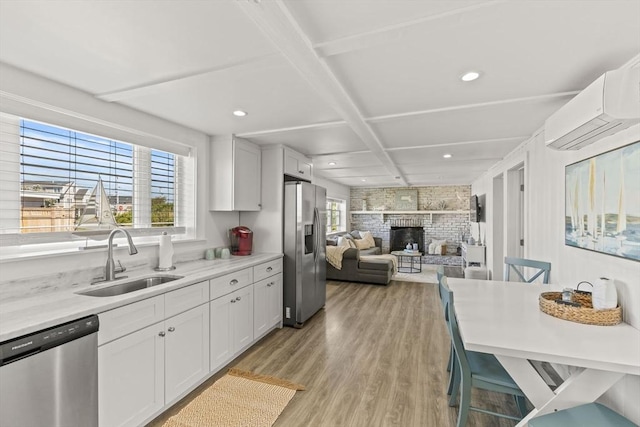 kitchen with appliances with stainless steel finishes, a sink, a wall mounted air conditioner, light wood finished floors, and light countertops