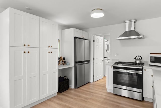 4 Agawam Ave, Ipswich, MA 01938 - kitchen featuring stainless steel appliances, wall chimney exhaust hood, stacked washing machine and dryer, white cabinets, and light wood-type flooring