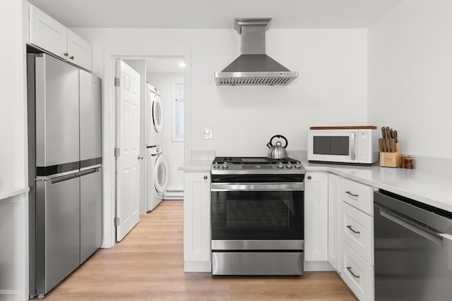 4 Agawam Ave, Ipswich, MA 01938 - kitchen featuring stainless steel appliances, wall chimney range hood, stacked washing machine and dryer, white cabinetry, and light countertops