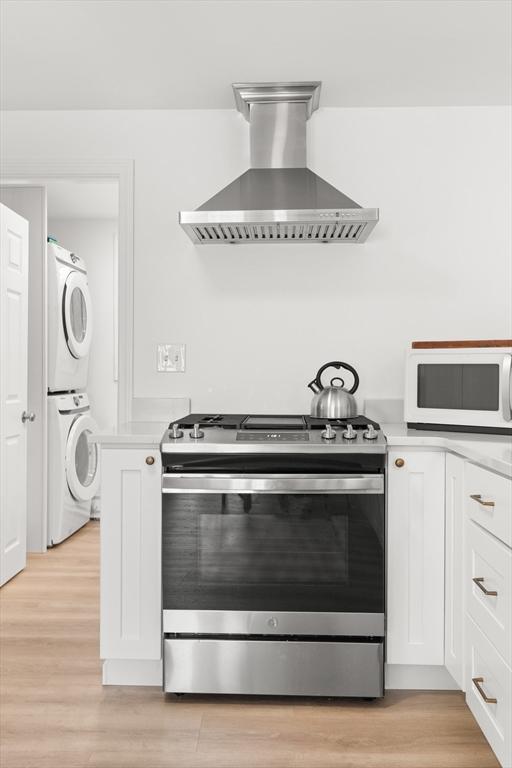 4 Agawam Ave, Ipswich, MA 01938 - kitchen featuring stainless steel gas stove, wall chimney exhaust hood, stacked washing machine and dryer, white microwave, and light countertops