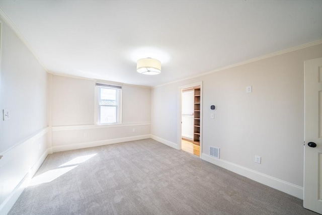 carpeted spare room featuring ornamental molding, visible vents, and baseboards