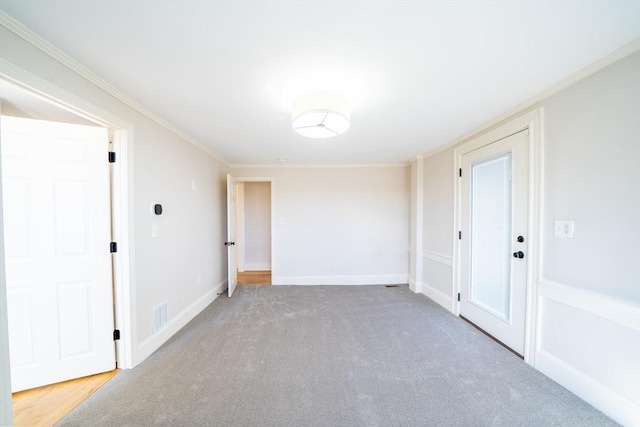 empty room with ornamental molding, carpet, visible vents, and baseboards