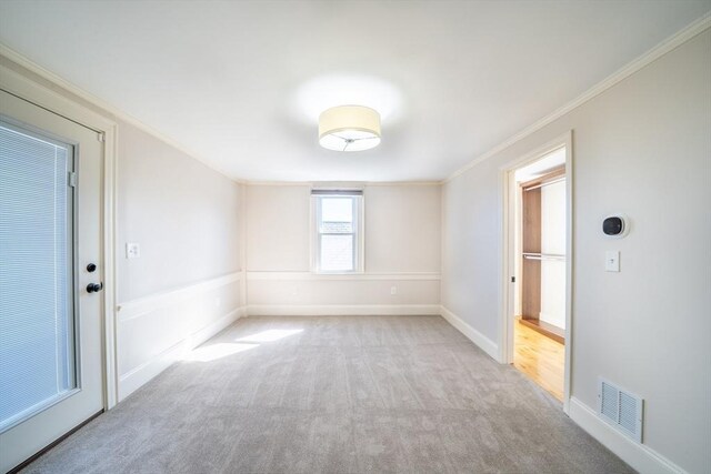 carpeted spare room featuring ornamental molding, visible vents, and baseboards