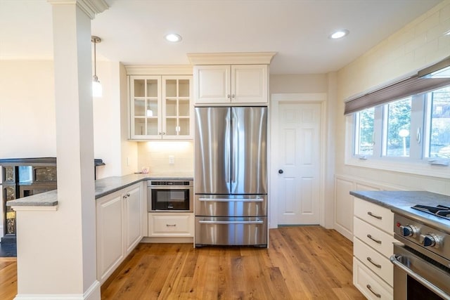 kitchen featuring decorative light fixtures, light wood finished floors, stainless steel appliances, glass insert cabinets, and a peninsula