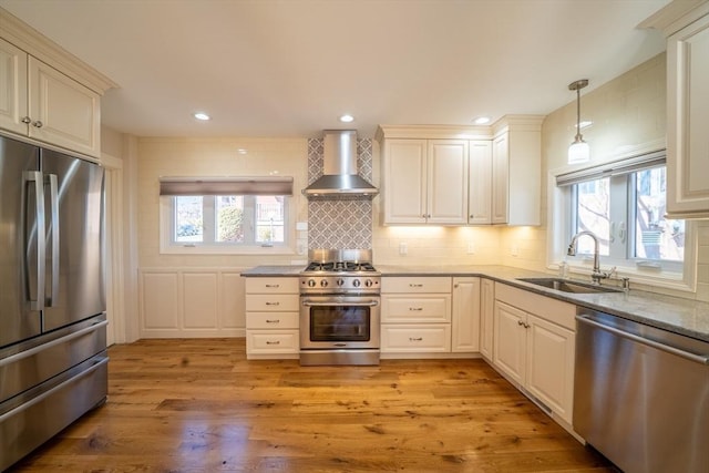 kitchen featuring tasteful backsplash, appliances with stainless steel finishes, light wood-style floors, a sink, and wall chimney exhaust hood