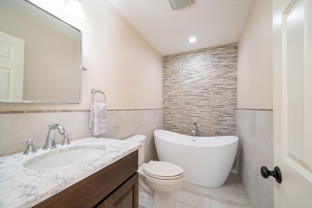 full bathroom with a wainscoted wall, tile walls, vanity, tile patterned flooring, and a freestanding tub