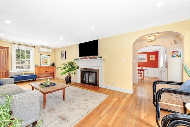 living room with crown molding, a fireplace, a wall mounted AC, and light wood-type flooring