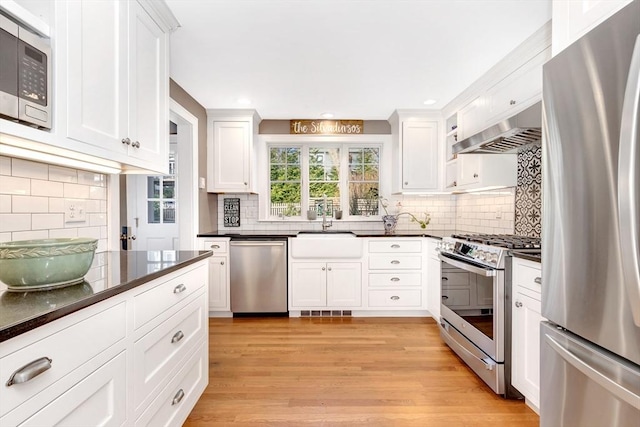 kitchen with white cabinetry, appliances with stainless steel finishes, sink, and range hood