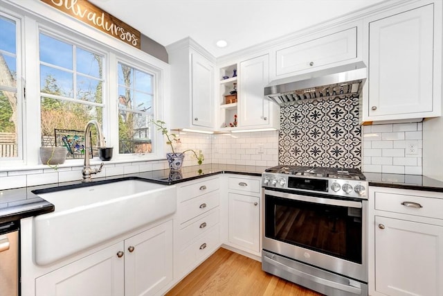 kitchen with appliances with stainless steel finishes, sink, white cabinets, light wood-type flooring, and wall chimney exhaust hood