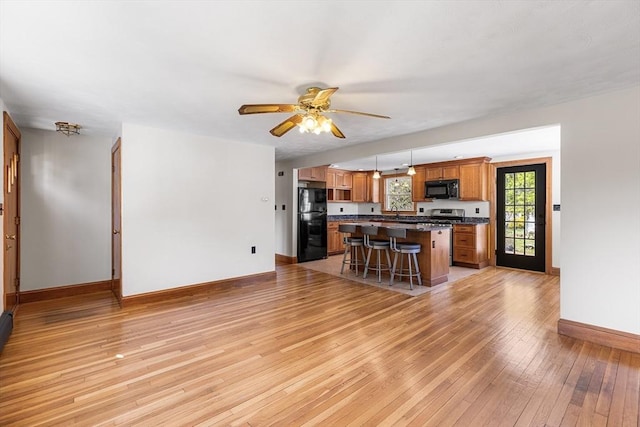 kitchen with dark countertops, baseboards, a kitchen breakfast bar, light wood-type flooring, and black appliances