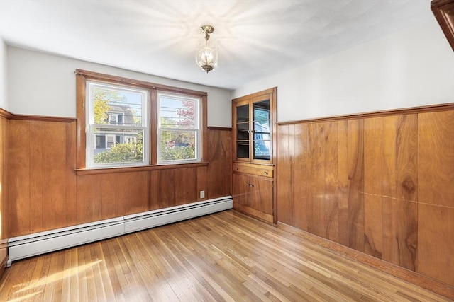 spare room featuring light wood-style flooring, wainscoting, a baseboard heating unit, and wood walls