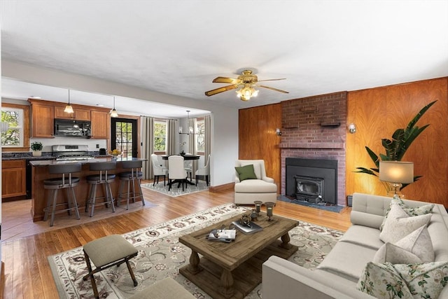 living area with ceiling fan, a wealth of natural light, a wood stove, and light wood-type flooring