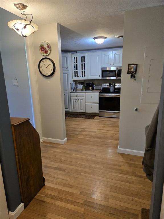 hallway featuring baseboards, light wood finished floors, and a textured ceiling