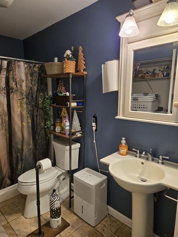 bathroom featuring toilet, baseboards, and curtained shower