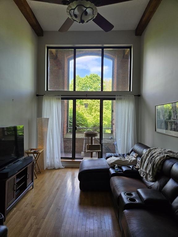 living area featuring beamed ceiling, hardwood / wood-style flooring, and a ceiling fan
