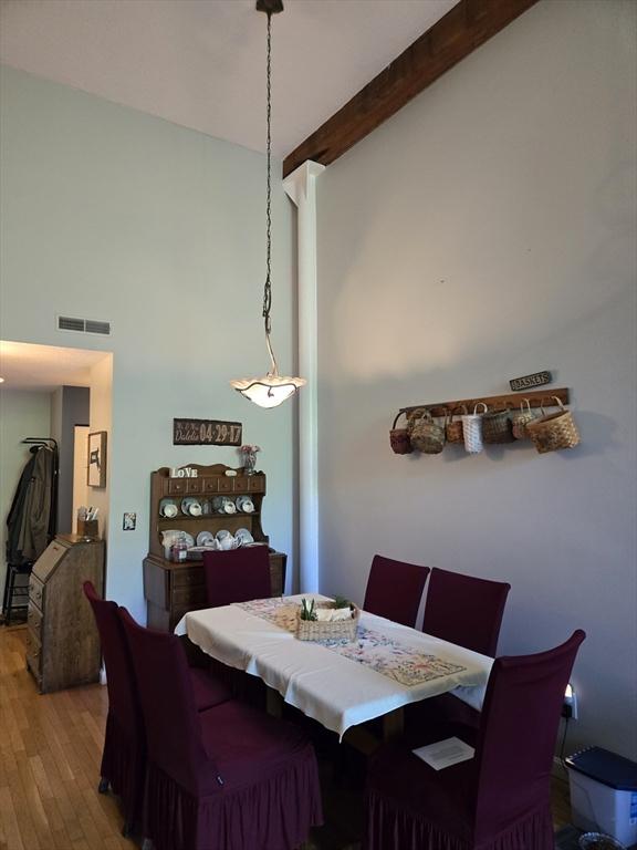 dining room featuring wood finished floors, a towering ceiling, and beam ceiling