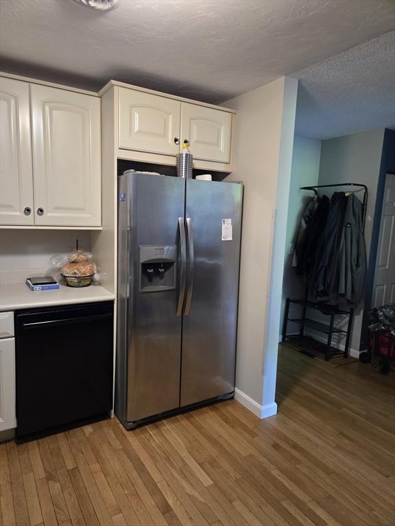 kitchen with stainless steel fridge, black dishwasher, light wood-type flooring, white cabinets, and baseboards