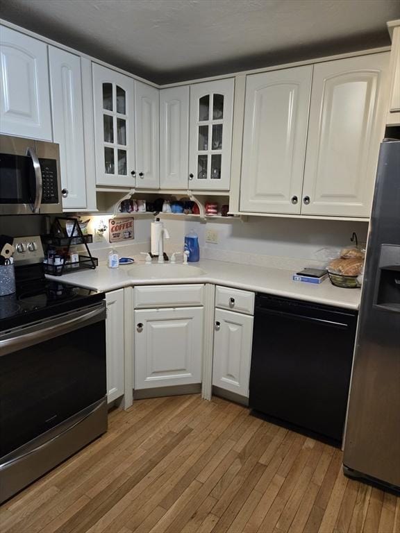 kitchen with stainless steel appliances, light wood-style floors, white cabinets, glass insert cabinets, and light countertops
