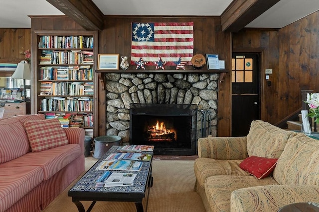 living room featuring wood walls, beamed ceiling, and a stone fireplace