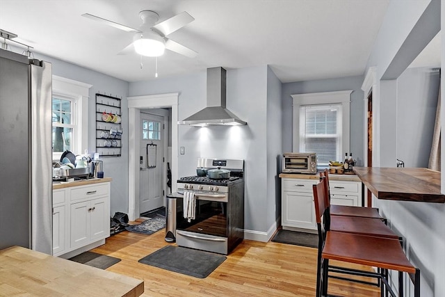 kitchen with white cabinets, light hardwood / wood-style flooring, stainless steel gas range, wall chimney exhaust hood, and butcher block countertops