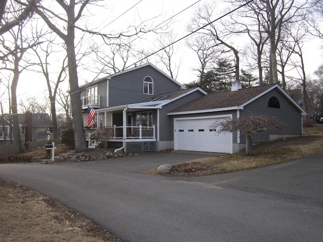 view of front of house featuring covered porch, a shingled roof, a chimney, a garage, and aphalt driveway