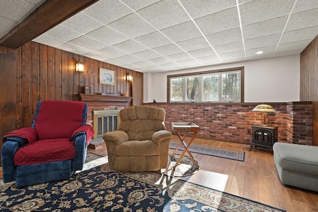 living room with wood walls, wood-type flooring, brick wall, and a wood stove