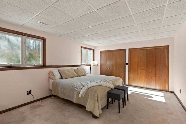 bedroom with multiple closets, light colored carpet, and a drop ceiling