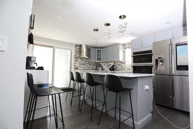 kitchen featuring decorative light fixtures, light countertops, wall chimney range hood, stainless steel fridge, and glass insert cabinets