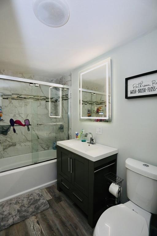 full bath featuring enclosed tub / shower combo, vanity, toilet, and wood finished floors