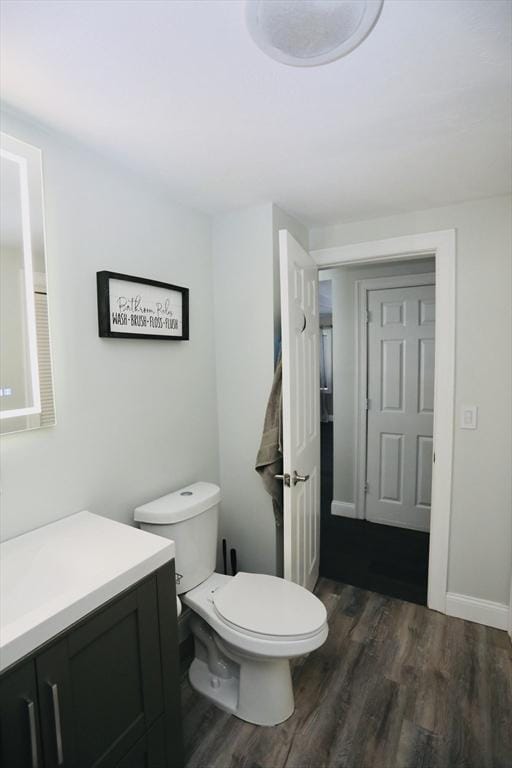 half bath with baseboards, vanity, toilet, and wood finished floors