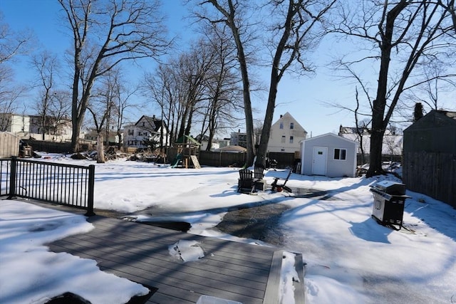 yard layered in snow featuring a playground, a storage shed, an outdoor structure, fence, and a residential view
