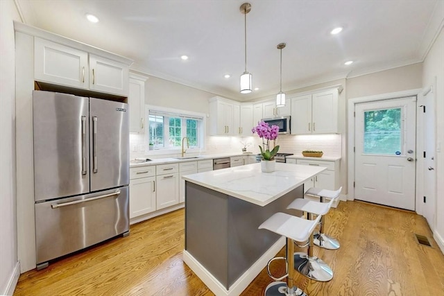 30 Pembroke St, Somerville, MA 02145 - kitchen featuring appliances with stainless steel finishes, white cabinets, crown molding, light wood finished floors, and tasteful backsplash