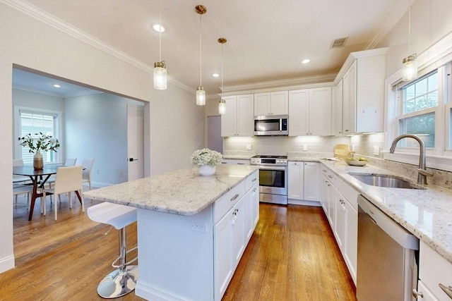 30 Pembroke St, Somerville, MA 02145 - kitchen with stainless steel appliances, a sink, wood finished floors, a kitchen island, and ornamental molding