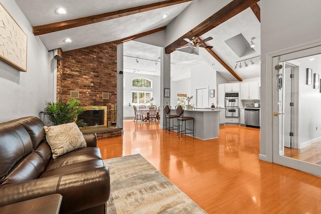 living area featuring baseboards, a fireplace, light wood-style flooring, beamed ceiling, and ceiling fan