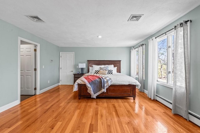 bedroom with visible vents, light wood-style flooring, and a baseboard heating unit