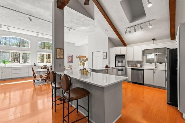 kitchen featuring white cabinets, appliances with stainless steel finishes, a kitchen breakfast bar, and light wood-style floors