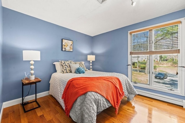 bedroom with a baseboard heating unit, baseboards, and wood finished floors