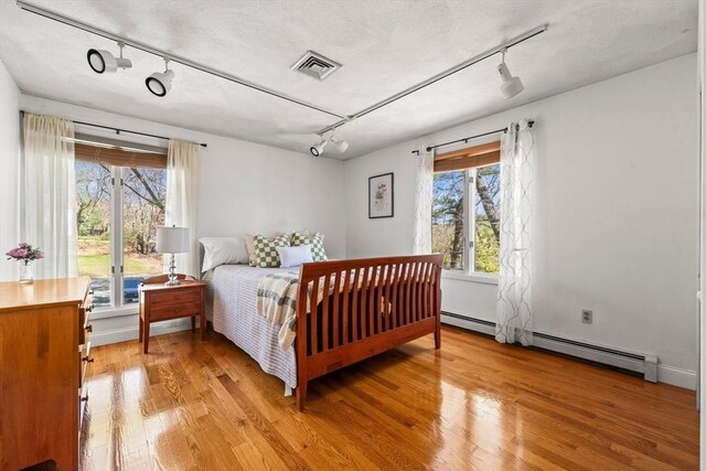 bedroom with light wood-type flooring, rail lighting, visible vents, and a textured ceiling