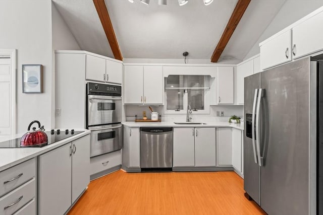 kitchen with stainless steel appliances, light countertops, a sink, and lofted ceiling with beams