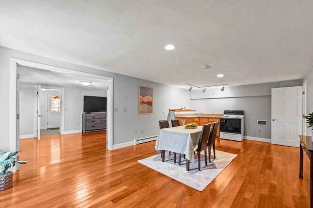 dining space with light wood-style floors, a baseboard heating unit, baseboards, and track lighting
