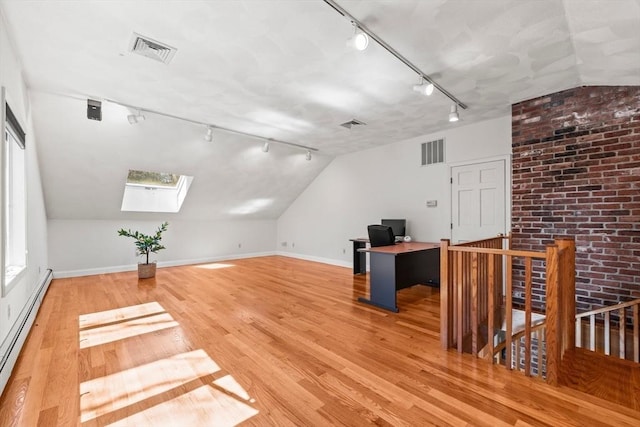 unfurnished office featuring light wood finished floors, visible vents, a baseboard radiator, and vaulted ceiling with skylight