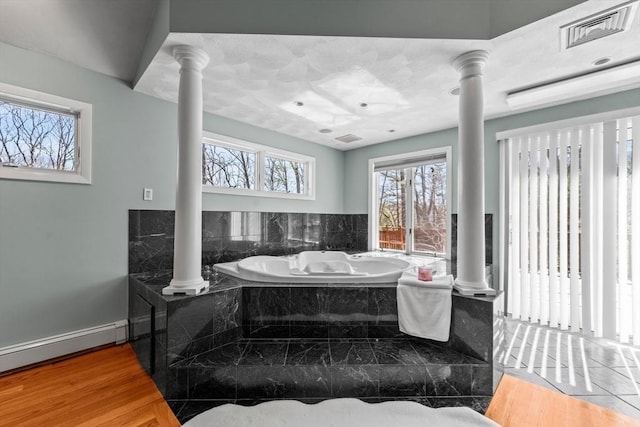 bathroom featuring visible vents, baseboard heating, ornate columns, wood finished floors, and a garden tub