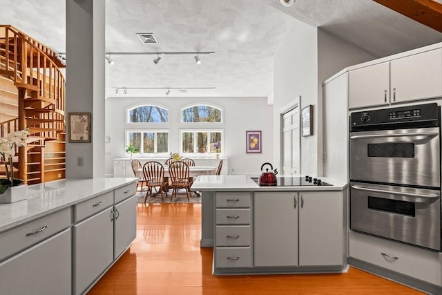 kitchen featuring black electric stovetop, a peninsula, light wood-style flooring, gray cabinetry, and stainless steel double oven