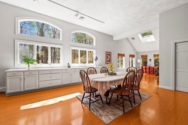 dining area featuring visible vents, light wood-type flooring, beamed ceiling, a skylight, and high vaulted ceiling