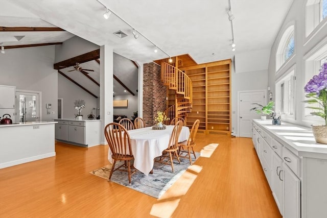 dining area with track lighting, stairway, ceiling fan, high vaulted ceiling, and light wood finished floors