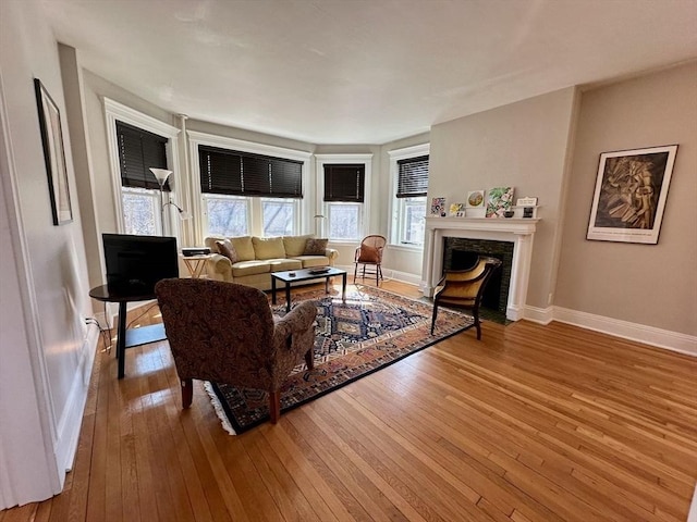 living area with a fireplace with flush hearth, baseboards, and hardwood / wood-style flooring