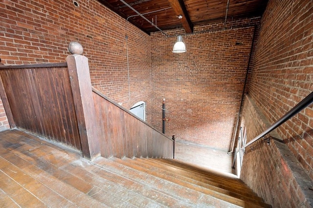 staircase featuring brick wall, beamed ceiling, hardwood / wood-style flooring, and wooden ceiling