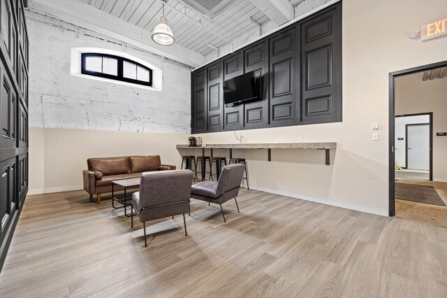 interior space featuring light wood-type flooring, beamed ceiling, and baseboards