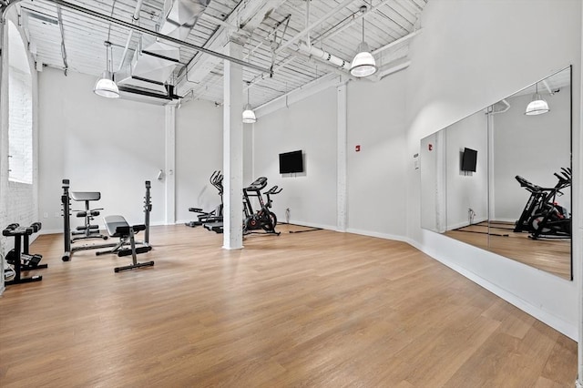 gym featuring a towering ceiling, baseboards, and wood finished floors