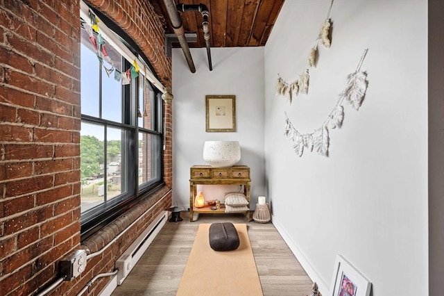 interior space featuring baseboards, wooden ceiling, brick wall, baseboard heating, and wood finished floors